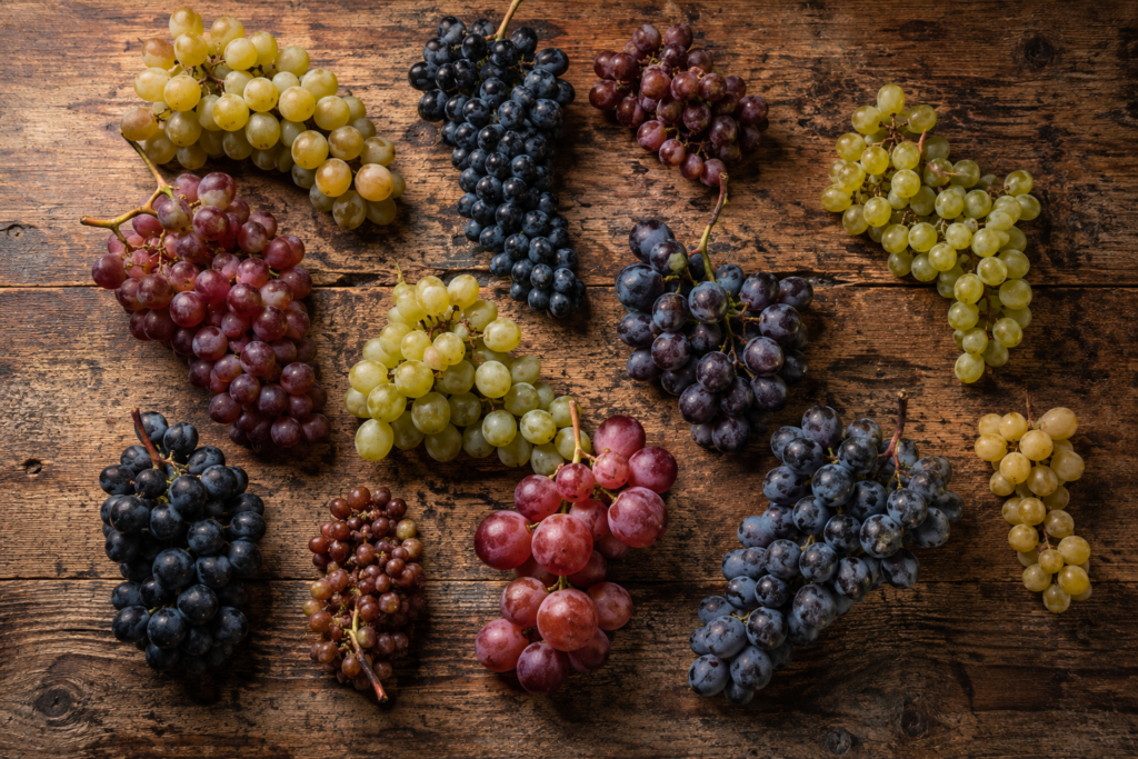Diferentes cachos de uvas de castas autóctones portuguesas sobre uma mesa de madeira rústica, ilustrando o artigo “Castas Autóctones: Património ou Discurso?”